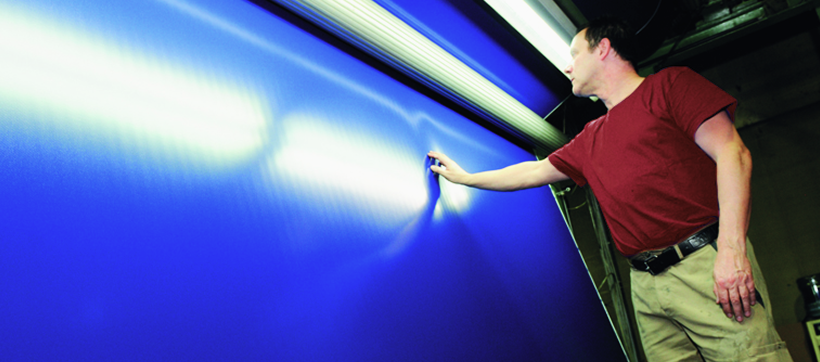 Technician inspecting a blue coated vinyl sheet for gloss and uniform thickness under lights